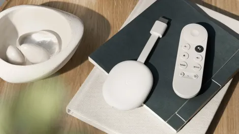 Chromecast with google tv hd and remote lays on top of two books on a coffee table with a decorative bowl nearby